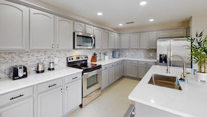 A modern kitchen with white cabinetry, a stainless steel refrigerator, a microwave, and a stove. - Dog-friendly Home With Lake Views, Ping-pong, air Hockey, Streaming, W/d, & AC (Kissimmee)