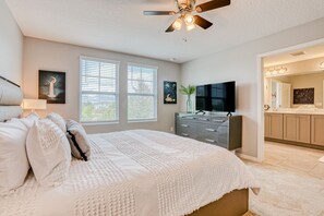A bedroom with a large bed, a ceiling fan, a dresser, a TV, and a bathroom visible through an open door. - Spacious Townhome With Heated Pool, Wifi, & Central A/C - Near Theme Parks (Davenport)