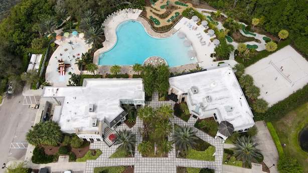 Vue aérienne d’un complexe hôtelier doté d’une piscine, d’espaces de détente et d’un court de tennis.