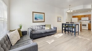 A modern living room with a gray sofa, a dining area with a table and chairs, and a kitchen with wooden cabinets and a microwave. - Snowbird-friendly Condo Near Disney and Orlando With Outdoor Pool, Fast Wifi, W/D (Kissimmee)