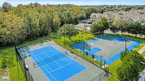 A tennis court with a fence, surrounded by trees and residential buildings. - Snowbird-friendly Condo Near Disney and Orlando With Outdoor Pool, Fast Wifi, W/D (Kissimmee)