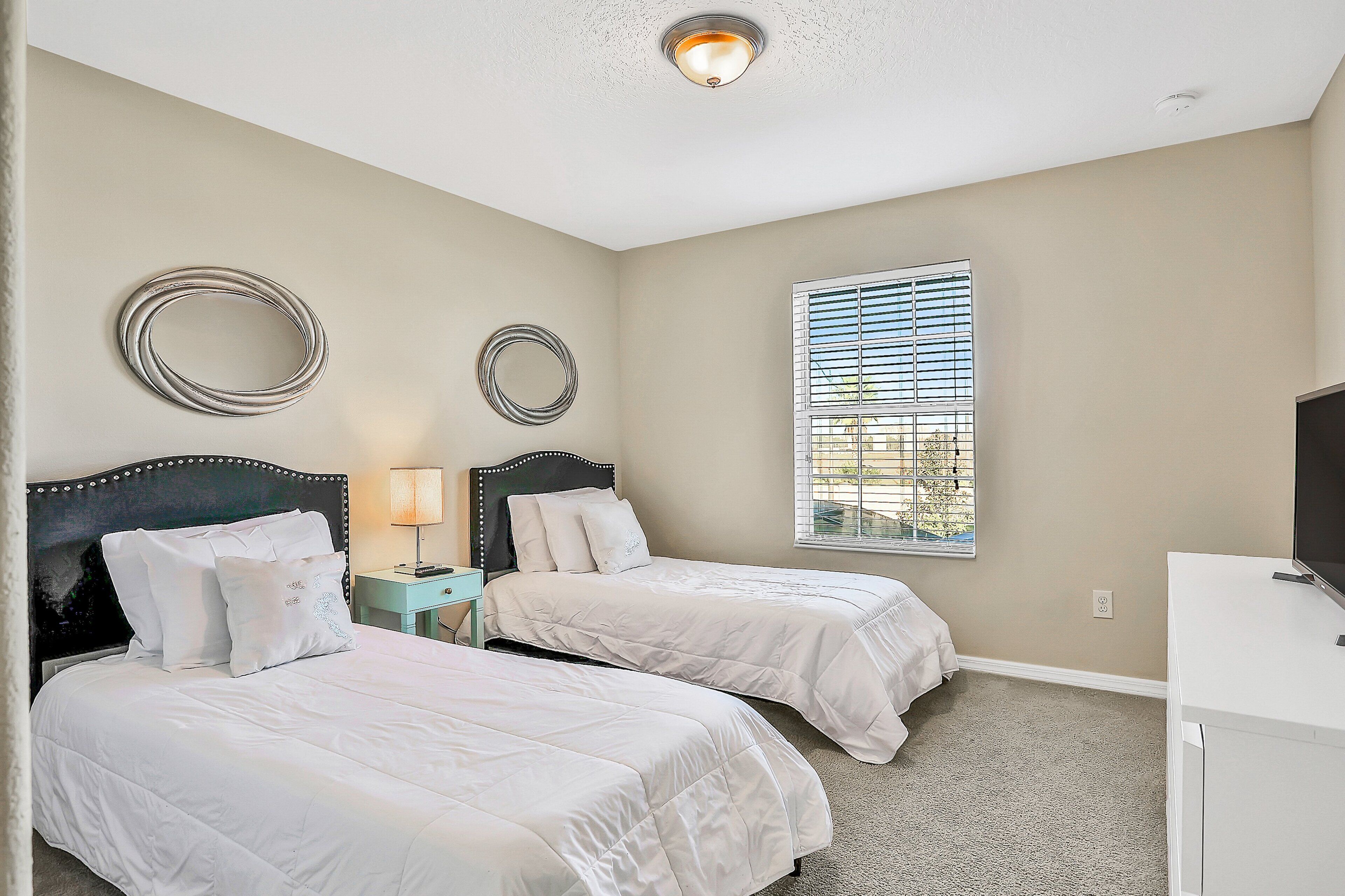 A bedroom with two beds, a nightstand, a TV, and a window with blinds.