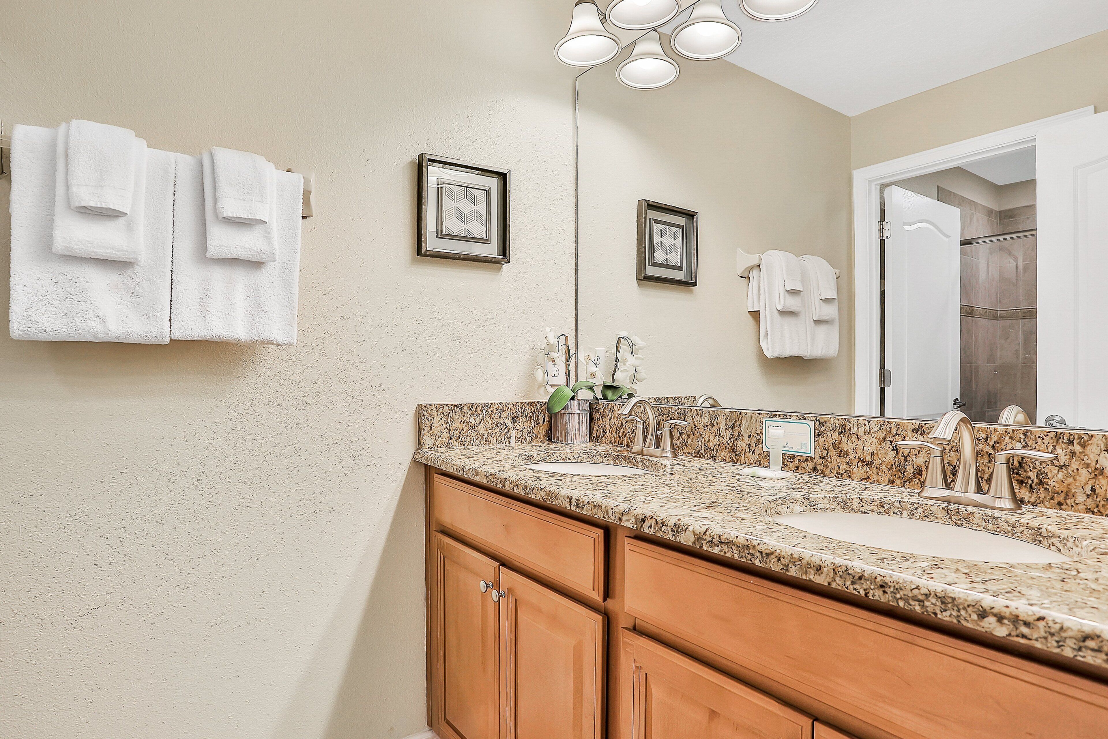 A bathroom with a granite countertop, double sink, wooden cabinets, and a large mirror.