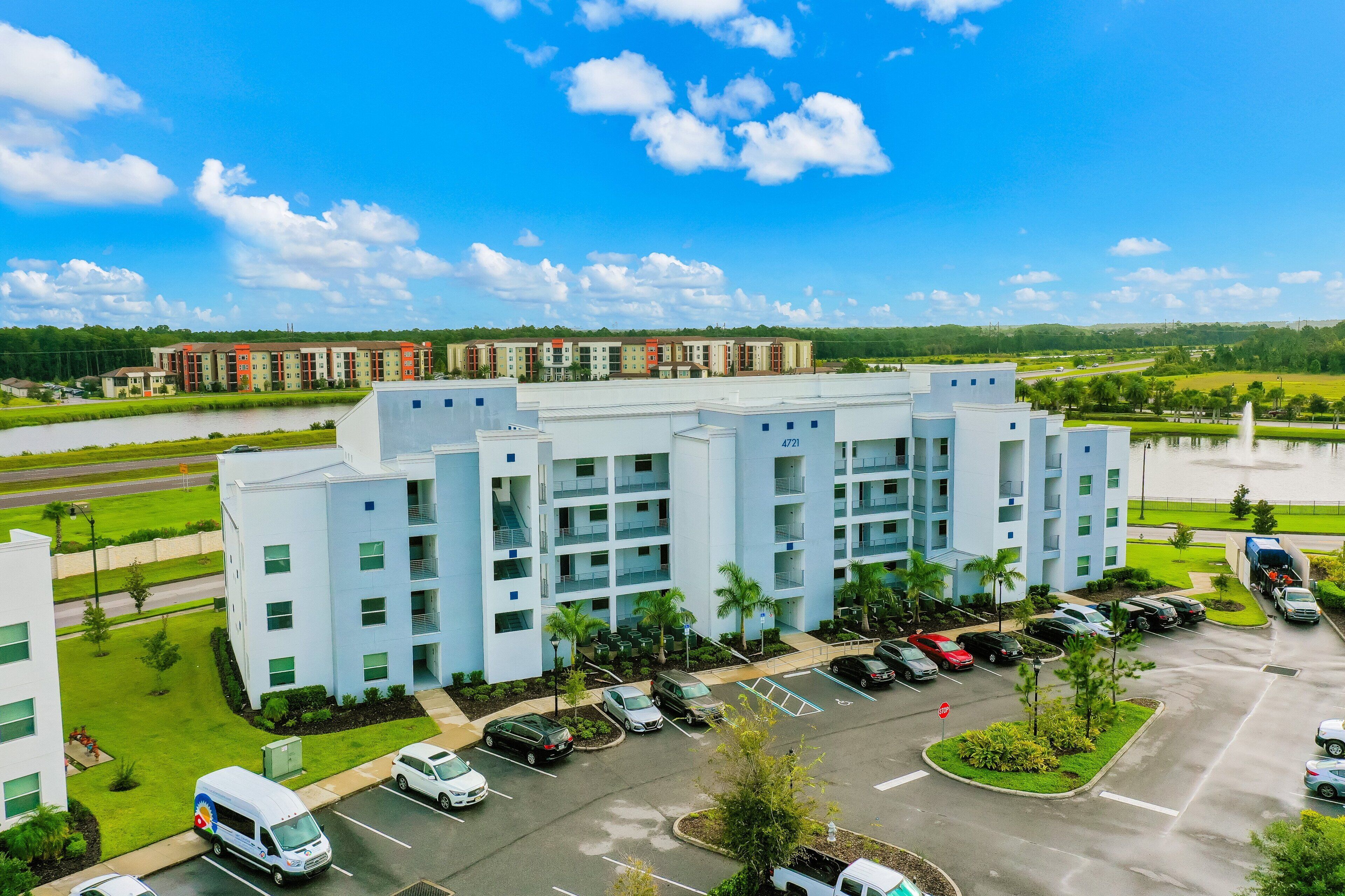 A multi-story hotel with a parking lot, a river in the background, and a clear sky.