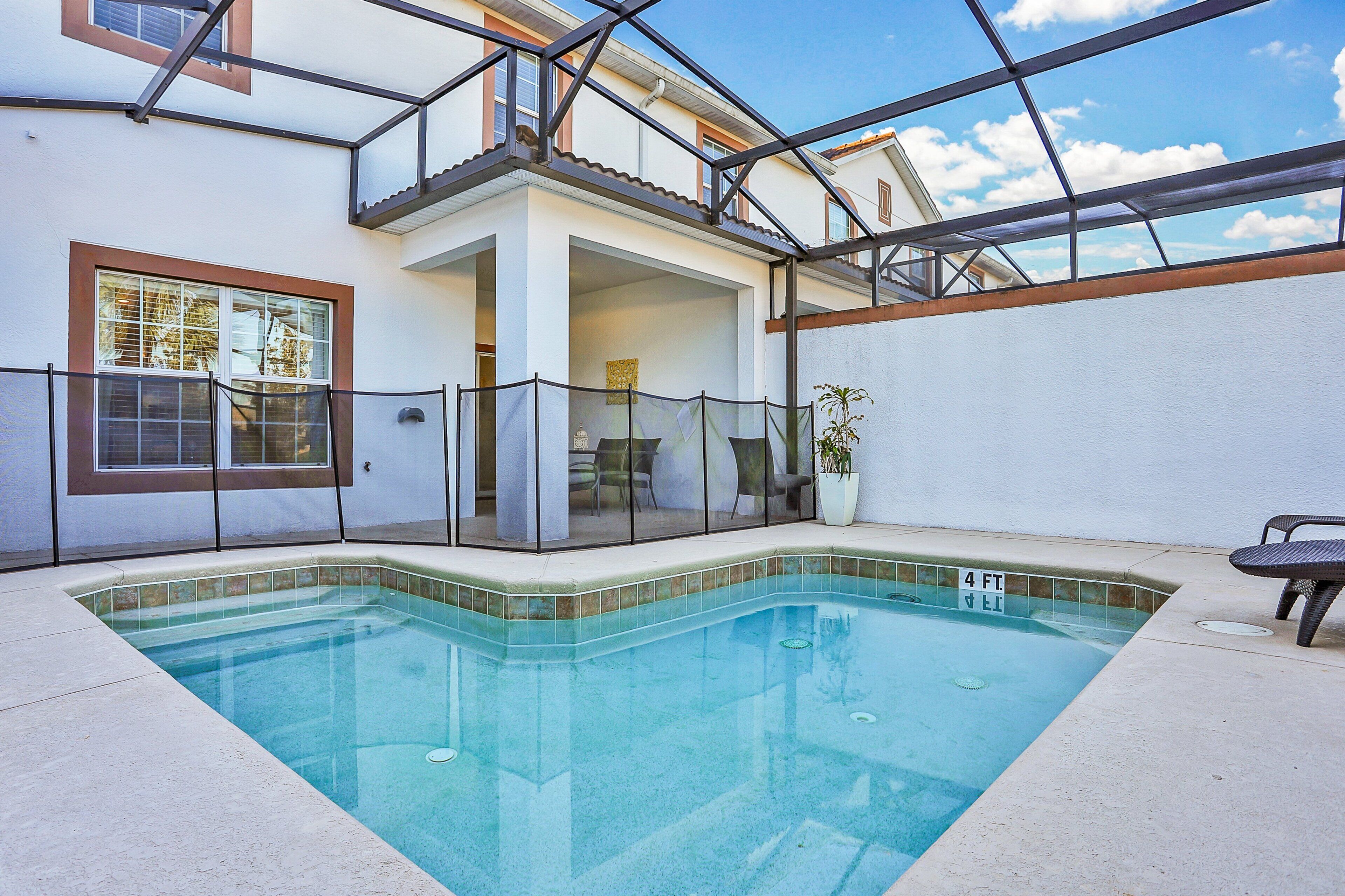 Une piscine dont la profondeur maximale est indiquée à 4 pieds, un patio couvert et une vue sur un immeuble résidentiel.