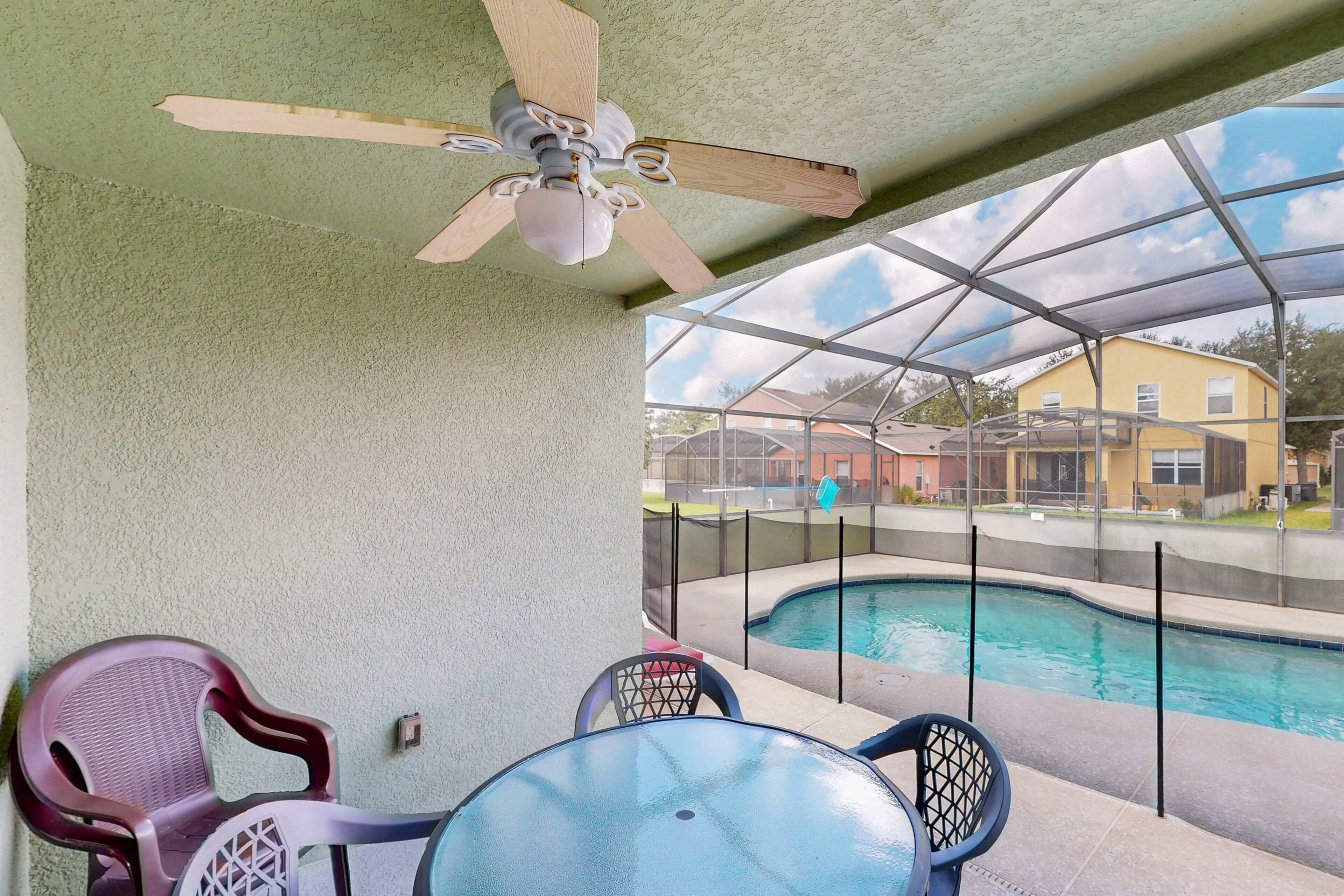 Área externa coberta com ventilador de teto, piscina e vista para uma casa amarela.