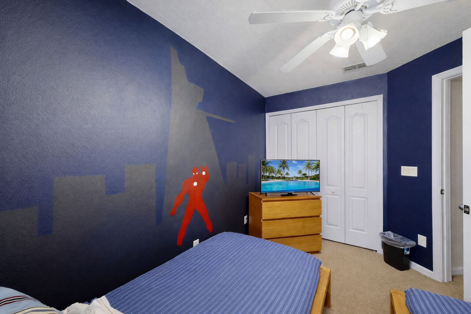 A bedroom with two beds, a TV on a wooden dresser, a ceiling fan, and a door.