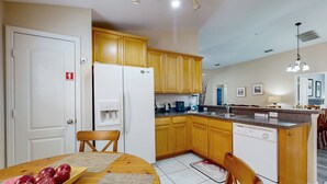 Una cocina con armarios de madera, un refrigerador blanco, una mesa de comedor con manzanas y un lavavajillas.