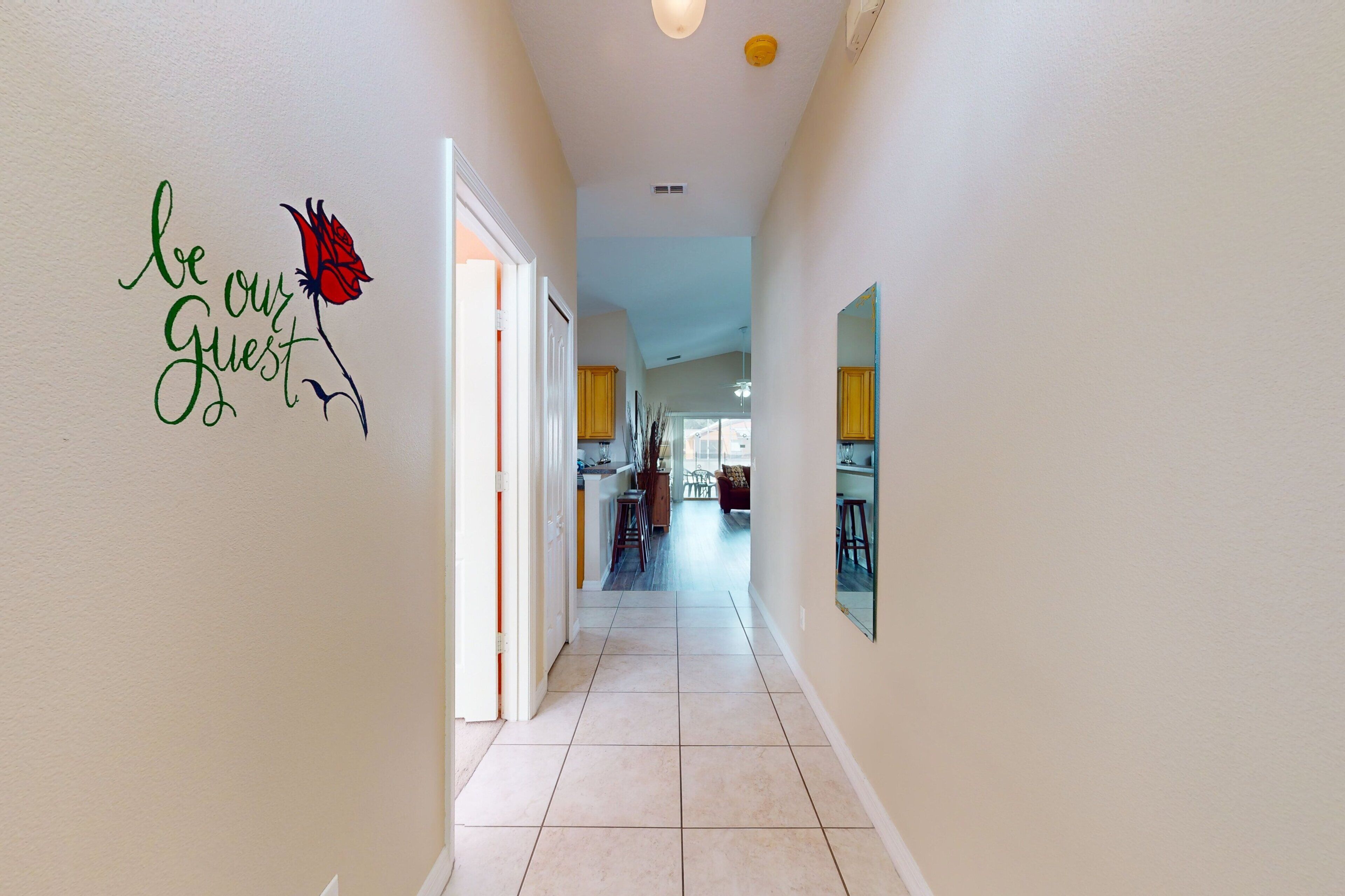 A hallway with a 'be our guest' sign, leading to a kitchen area.