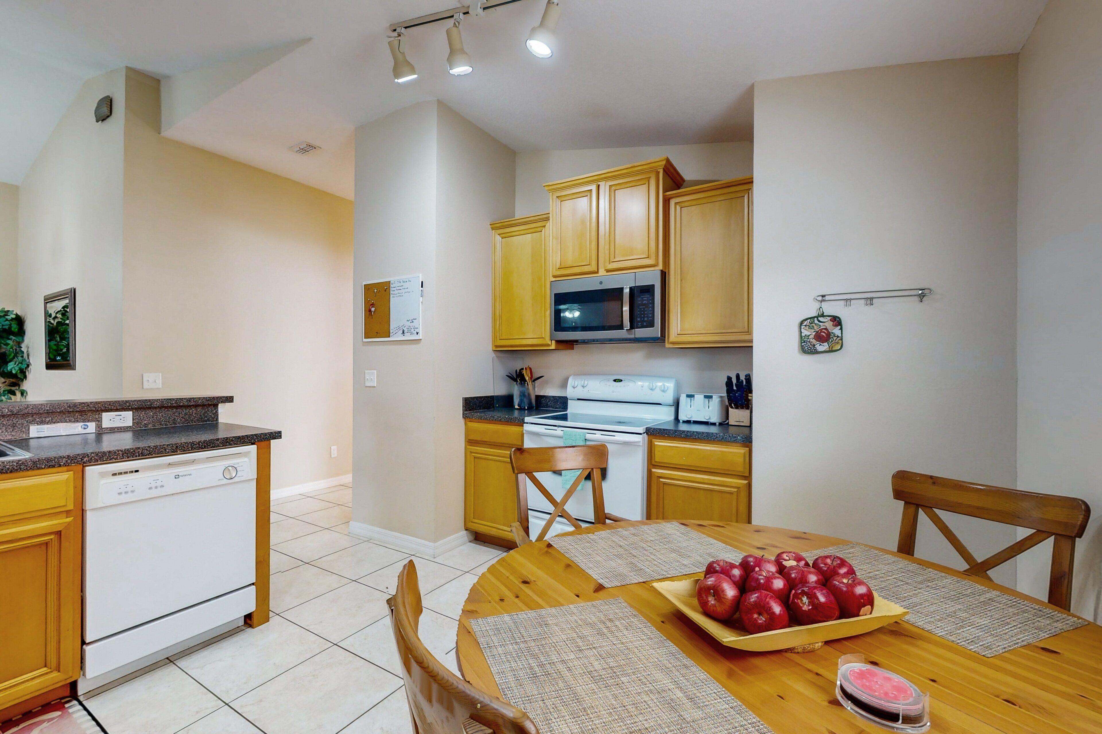 A kitchen with wooden cabinets, a microwave, and a dishwasher. There is a dining table with placemats and a plate of apples.