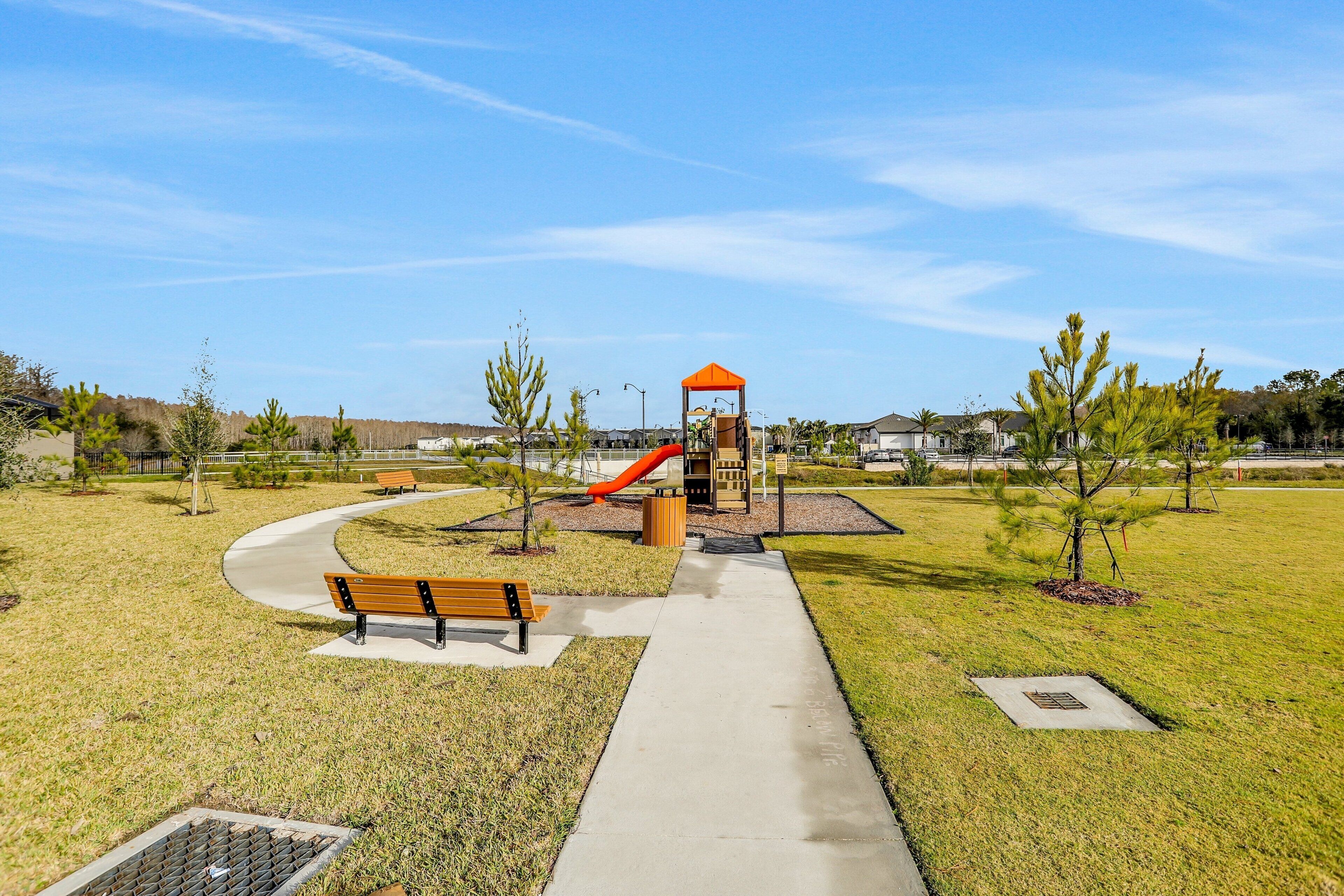 Ein Park mit Spielplatz, Bänken, einem gepflasterten Weg und Bäumen.