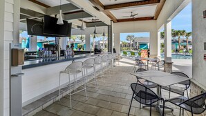 A covered outdoor bar area with a pool view, bar stools, and tables. - Stylish Townhouse With a Private Pool & Lanai Plus Clubhouse Amenities (Kissimmee)