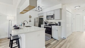 Una cocina moderna con armarios blancos, una isla central, electrodomésticos de acero inoxidable y una lámpara colgante.