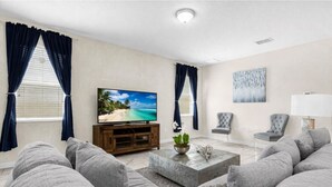 Una sala de estar con televisor, sofá, sillón, mesa de centro y un cuadro en la pared.