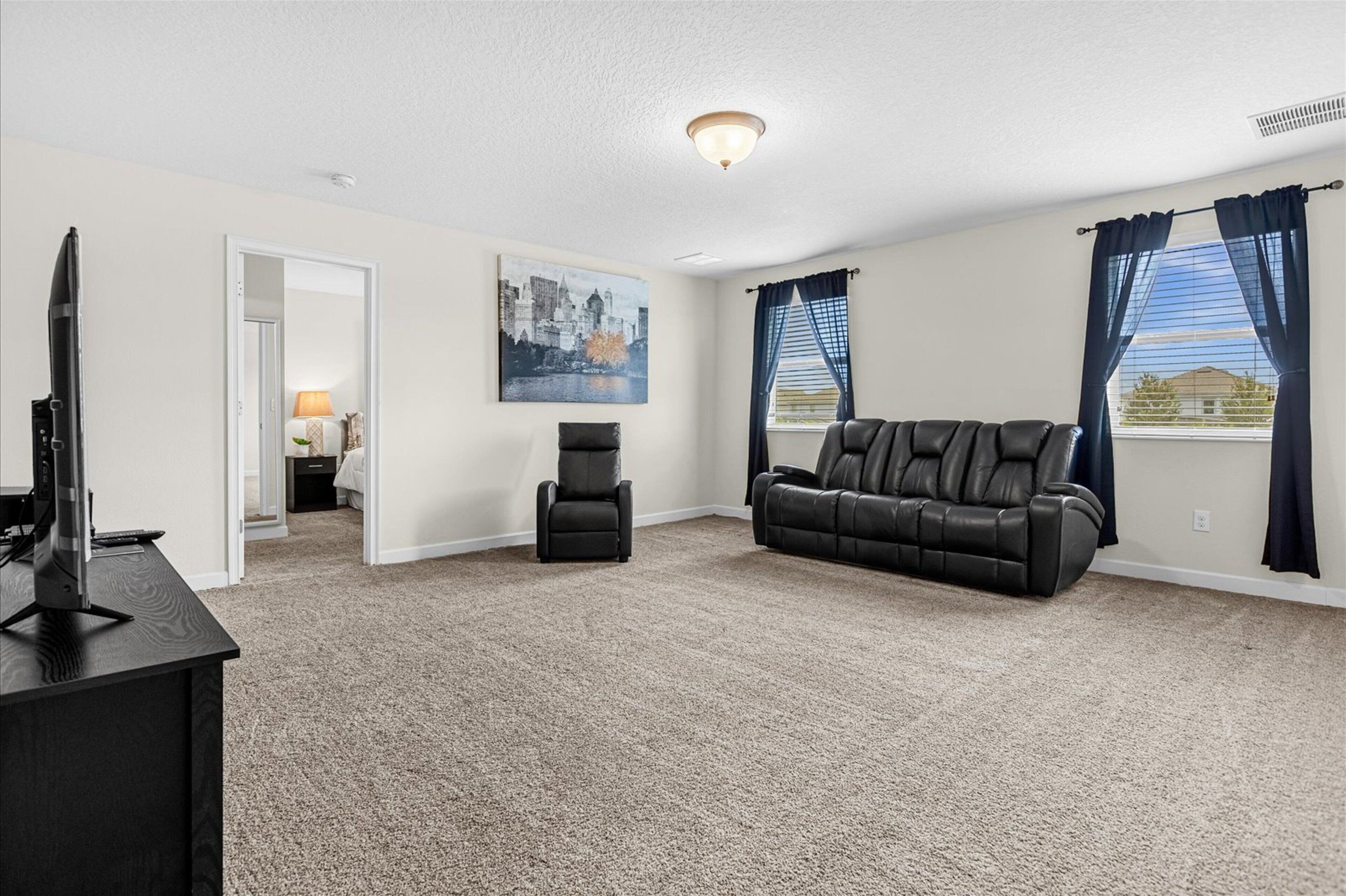 A spacious living room with a large black leather sofa, a recliner, a flat-screen TV, and a painting on the wall.