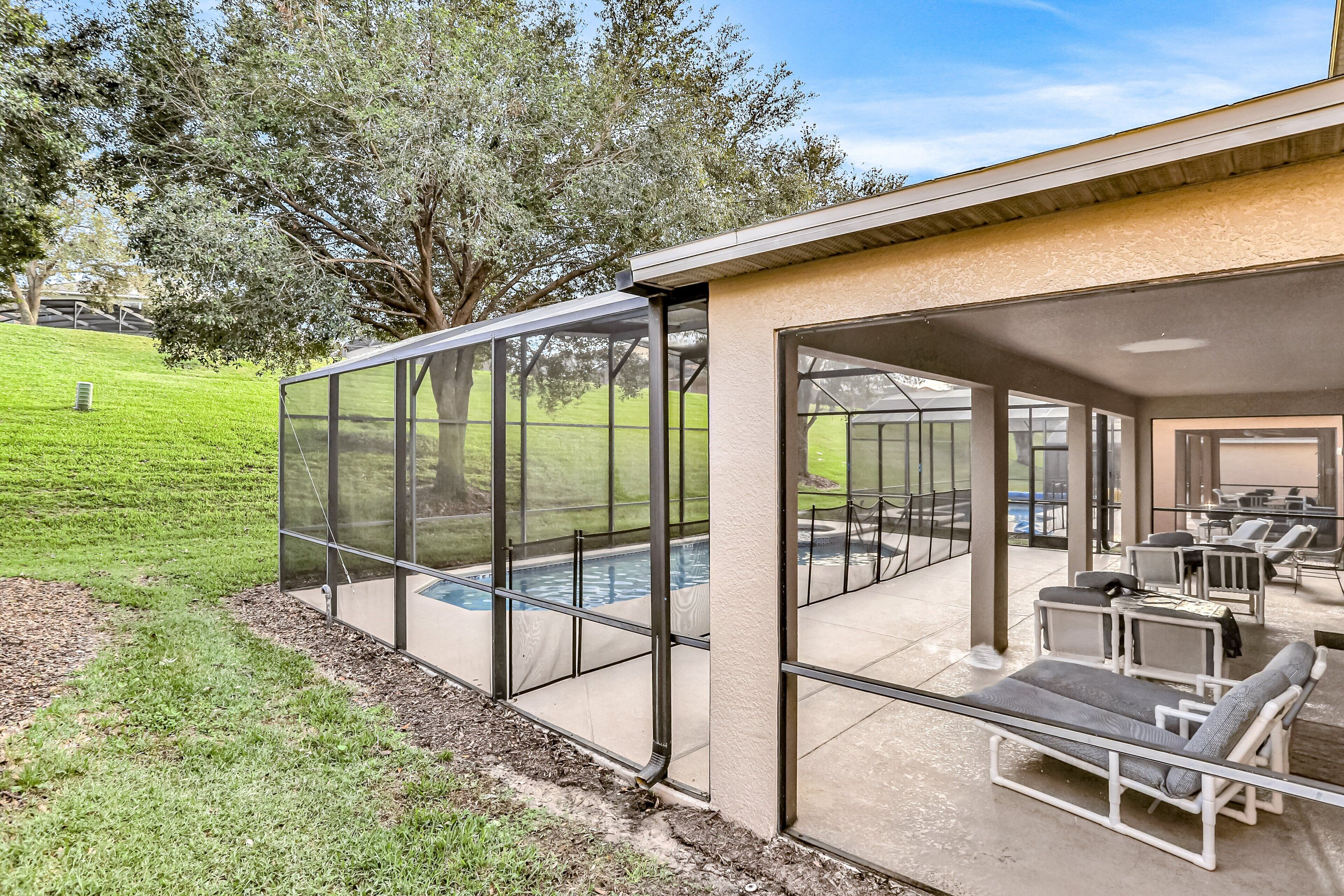 Un espacio exterior con paredes de vidrio, que incluye una piscina, sillas de descanso y una mesa de patio.