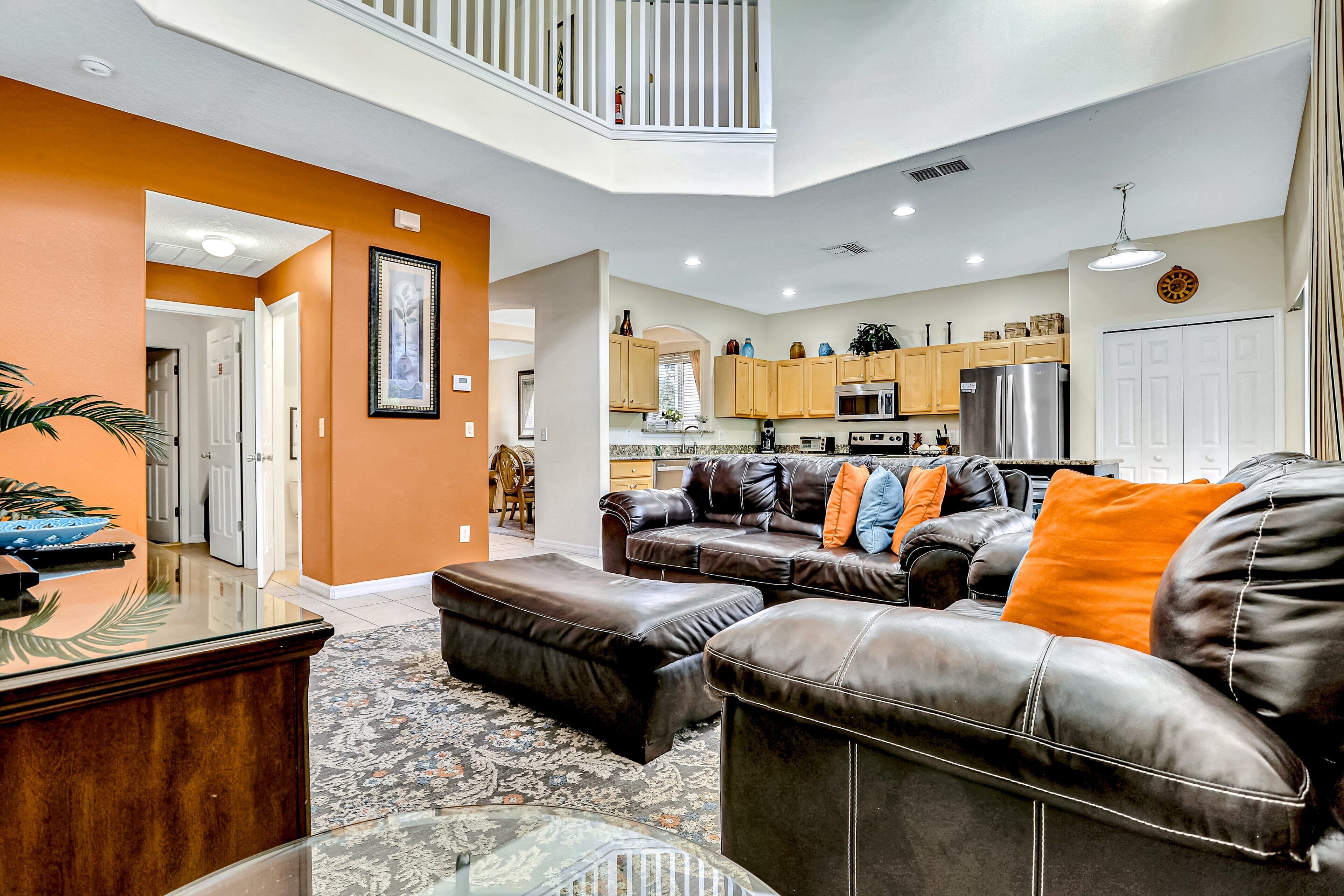 A spacious living area with a sectional sofa, a glass coffee table, and a dining area with a kitchen in the background.