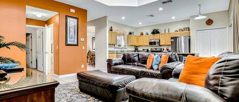 A spacious living area with a sectional sofa, a glass coffee table, and a dining area with a kitchen in the background.