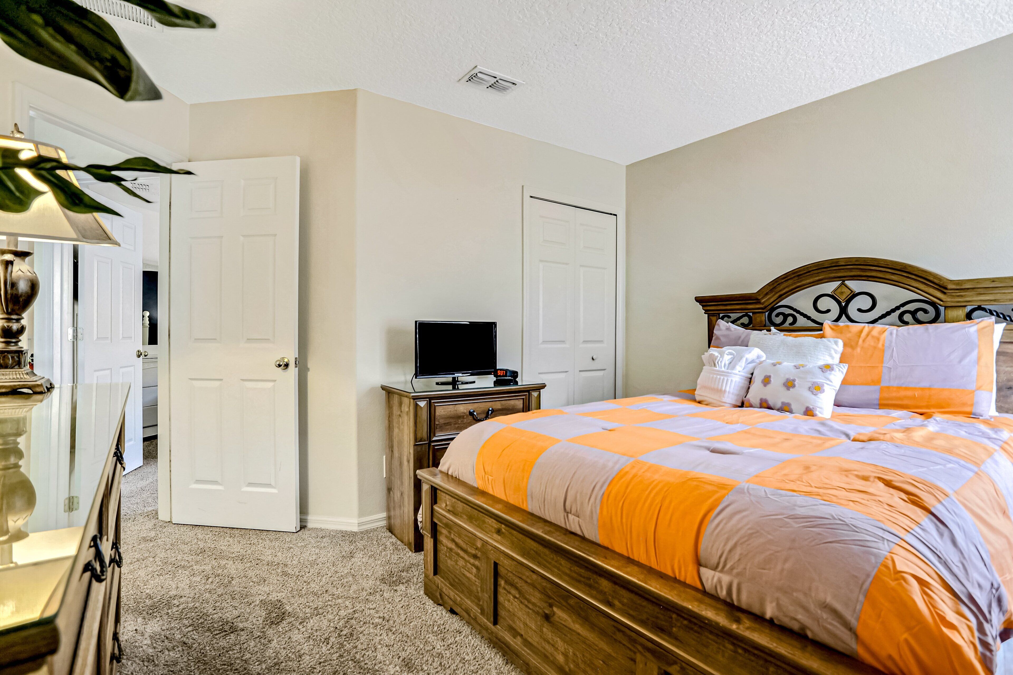 A bedroom with a wooden bed, a television on a stand, a dresser, and a door leading to another room.
