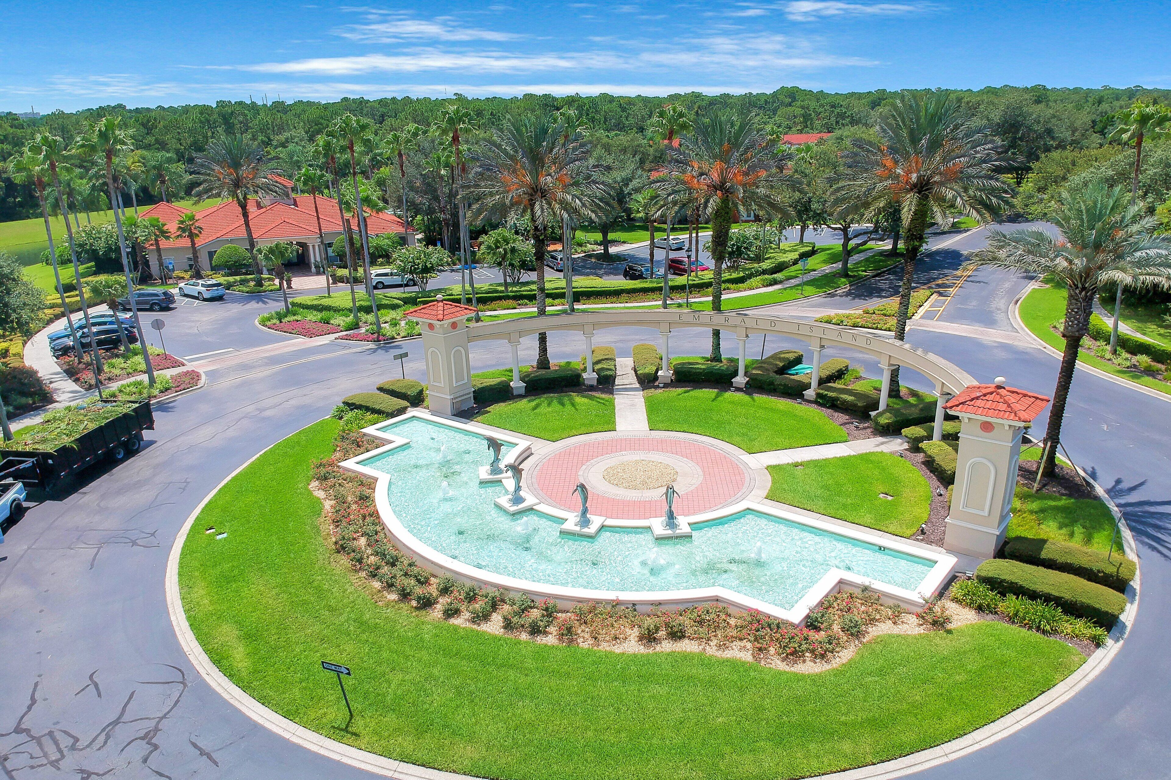 A landscaped area with a pool, palm trees, and a building with a red roof.