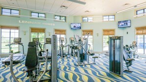 Un gimnasio con diferentes máquinas de ejercicio, ventanas amplias y una alfombra estampada.