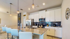 Una cocina moderna con armarios blancos, electrodomésticos de acero inoxidable y una isla central con taburetes de bar.