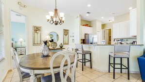A dining area with a wooden table and white chairs, a chandelier, and a kitchen with white cabinets and a refrigerator. - Dog-friendly Home w/ Private Pool, High-speed Wifi, and Central AC (Kissimmee)