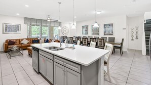 Cozinha moderna com ilha central, área de refeições com cadeiras e sala de estar com sofá e mesa de centro.