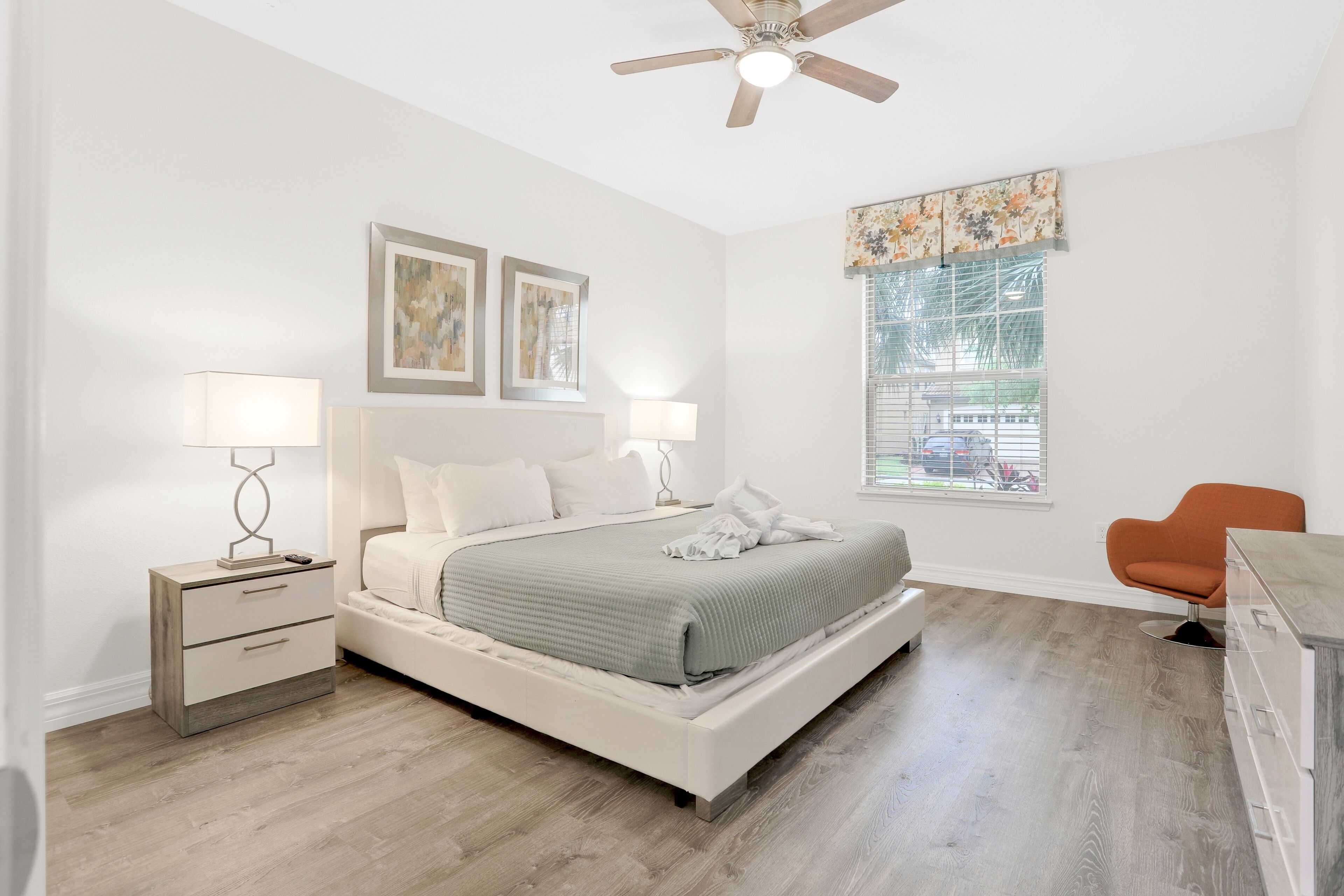A bedroom with a bed, nightstands, a ceiling fan, a window with blinds, and a chair.