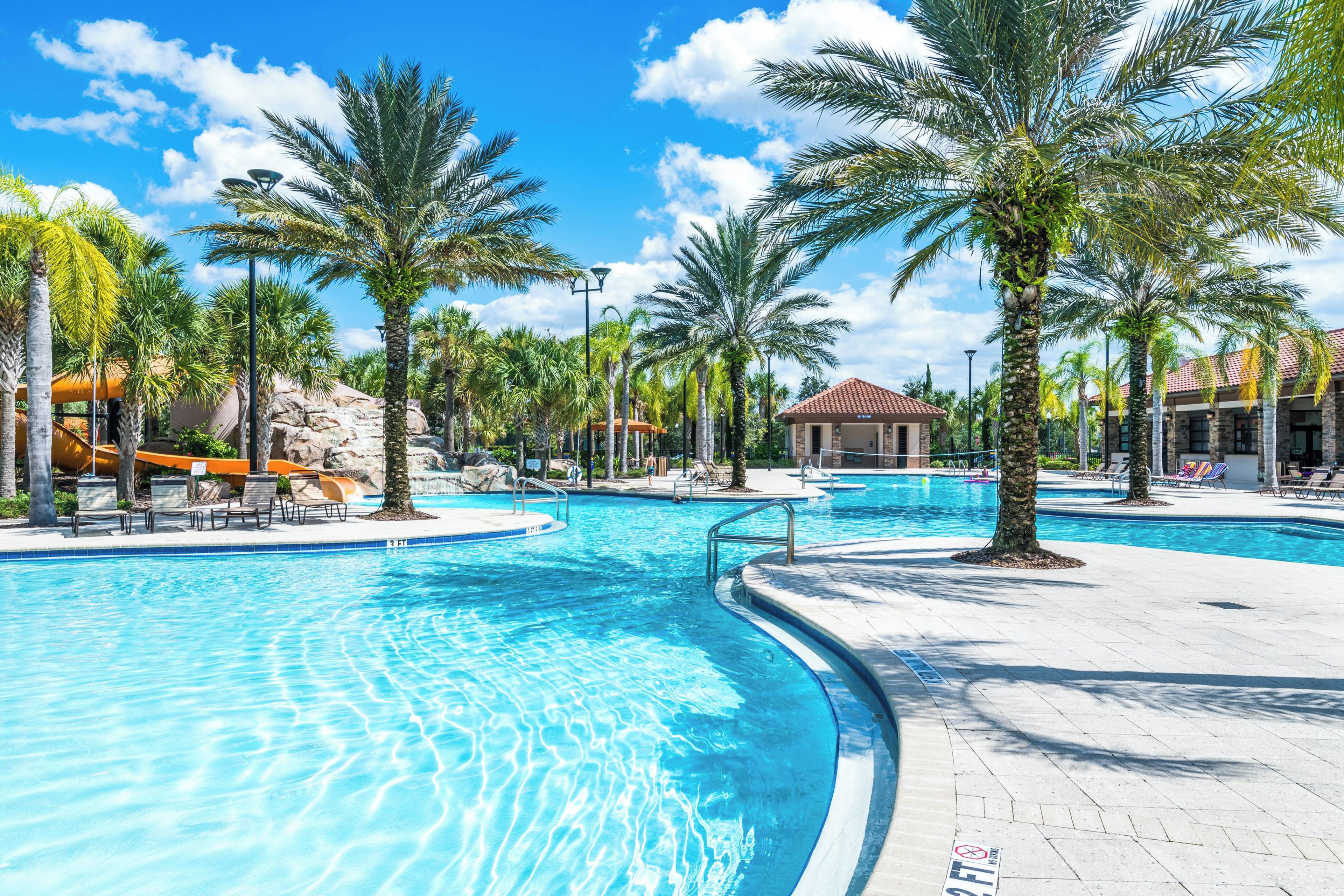 A large outdoor swimming pool with palm trees and lounge chairs.
