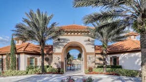 A gated entrance with a stone archway, palm trees, and a clear blue sky. - Family-friendly Home With Private Pool, spa & Resort Lazy River/water Slide (Davenport)