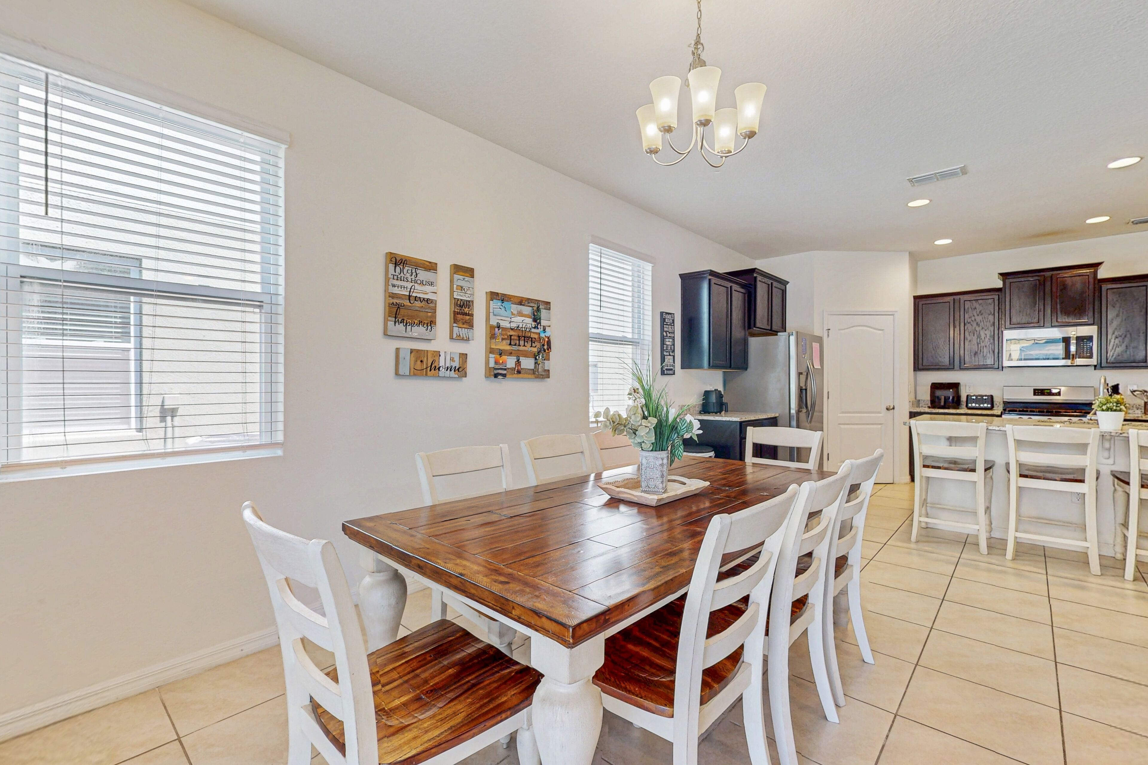 A spacious kitchen with white cabinetry, a wooden dining table, and a chandelier.