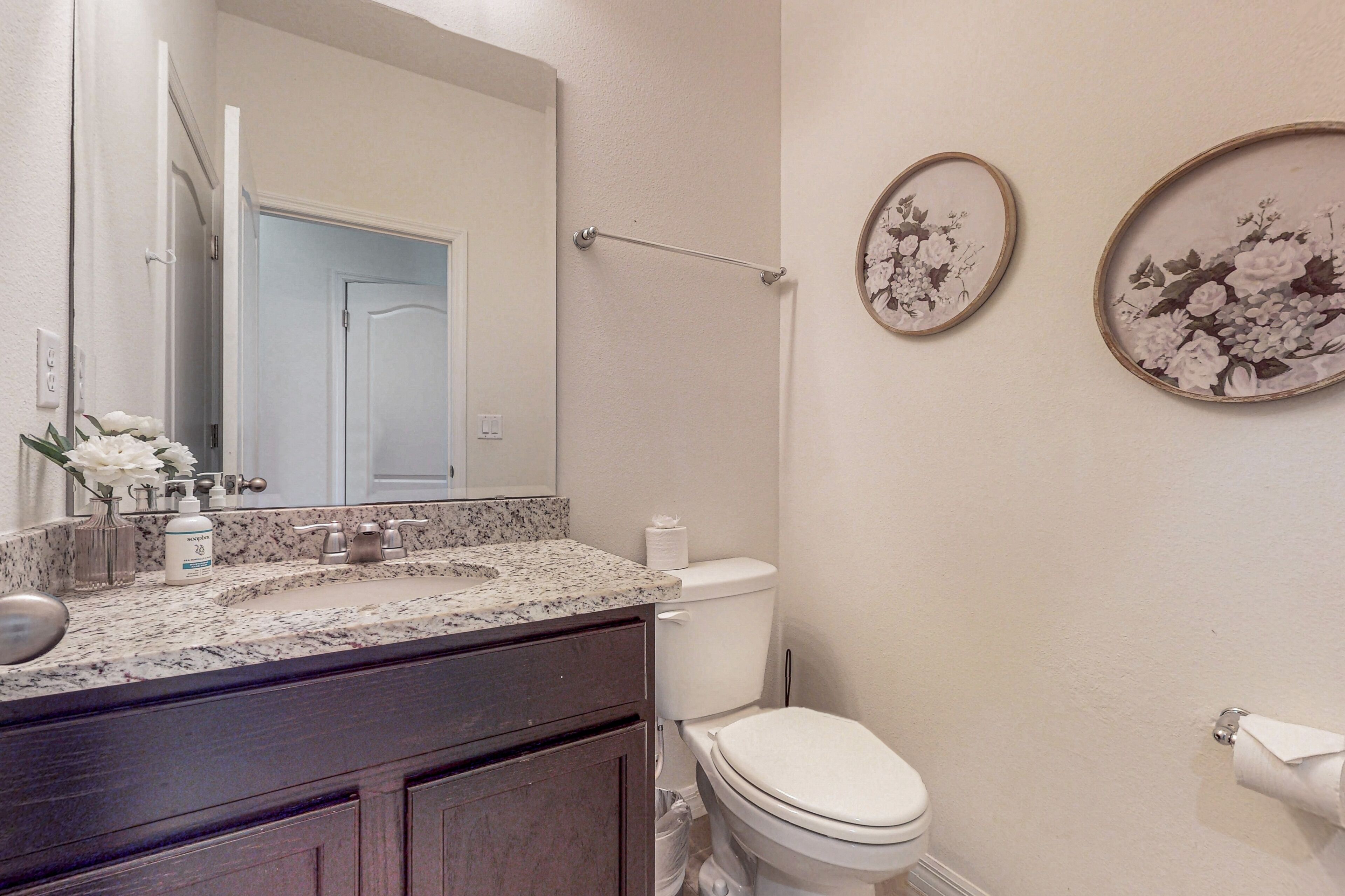 A bathroom with a granite countertop, a toilet, a towel rack, and two floral wall decorations.