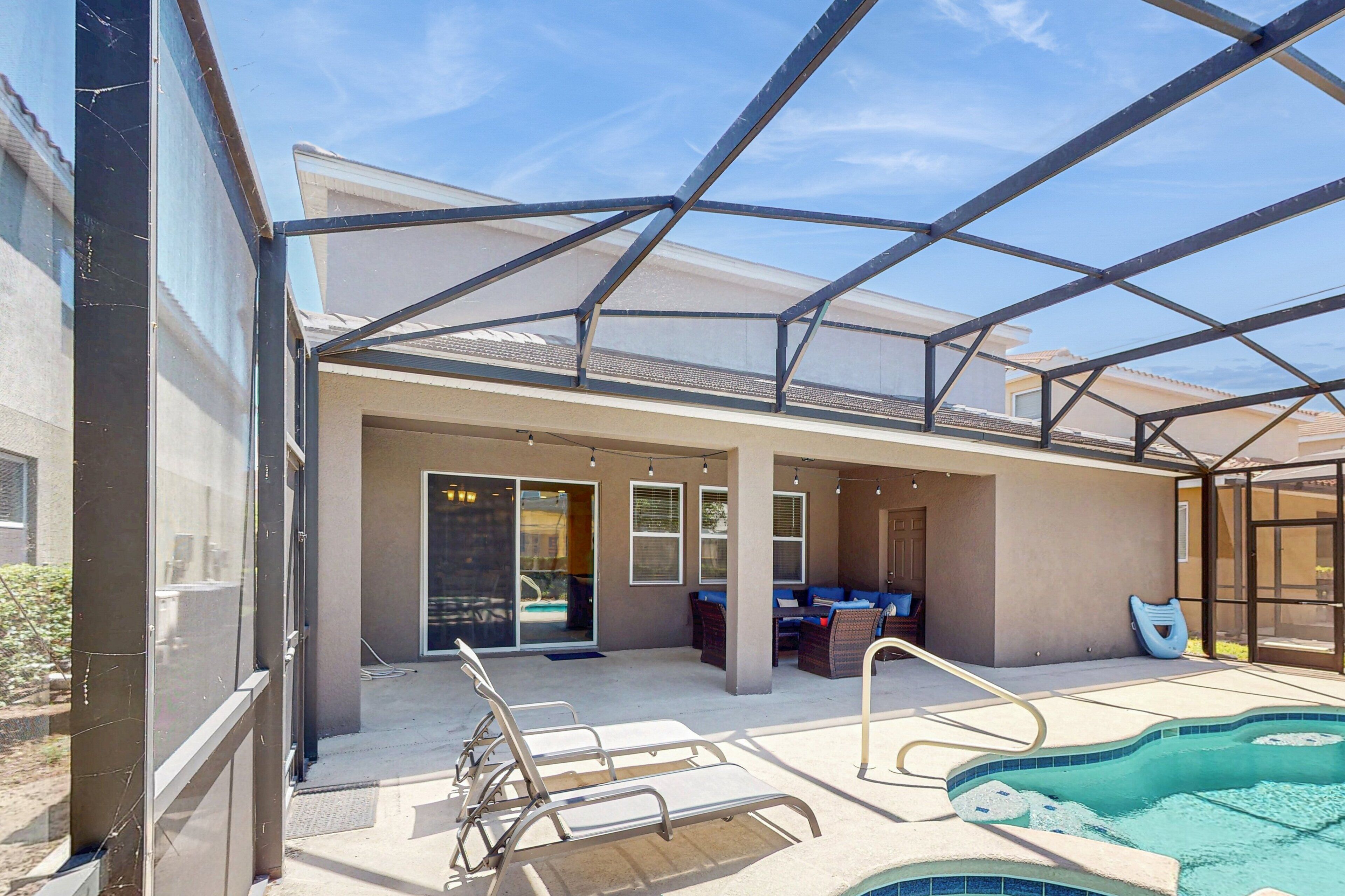 A covered outdoor area with a pool, lounge chairs, and a seating area.