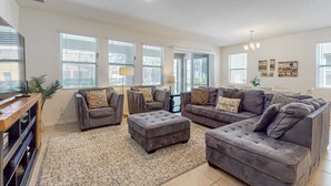 A spacious living room with grey sofas, a large ottoman, and a chandelier. - Family-friendly Home With Private Pool, spa & Resort Lazy River/water Slide (Davenport)