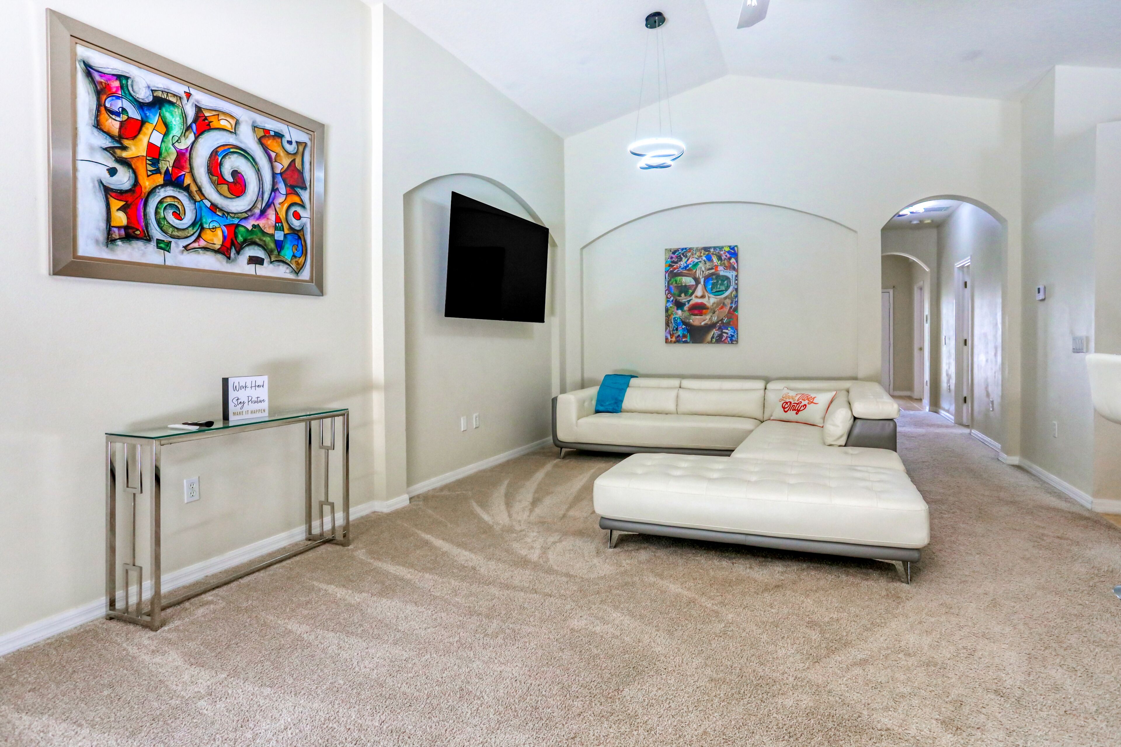 A spacious hallway with a white sofa, a glass console table, and two abstract paintings on the walls.