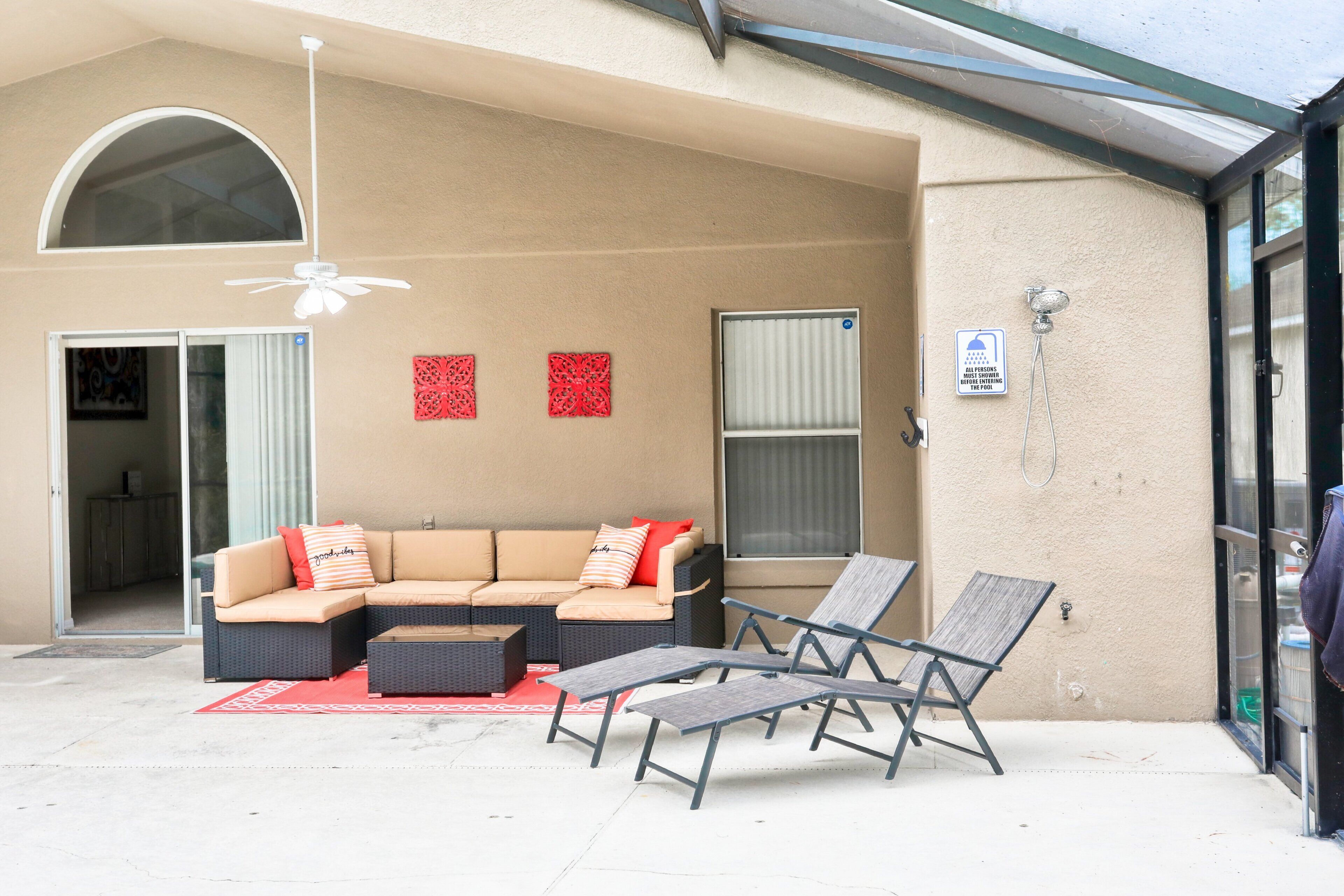 A covered outdoor seating area with a sofa, lounge chairs, and a ceiling fan.