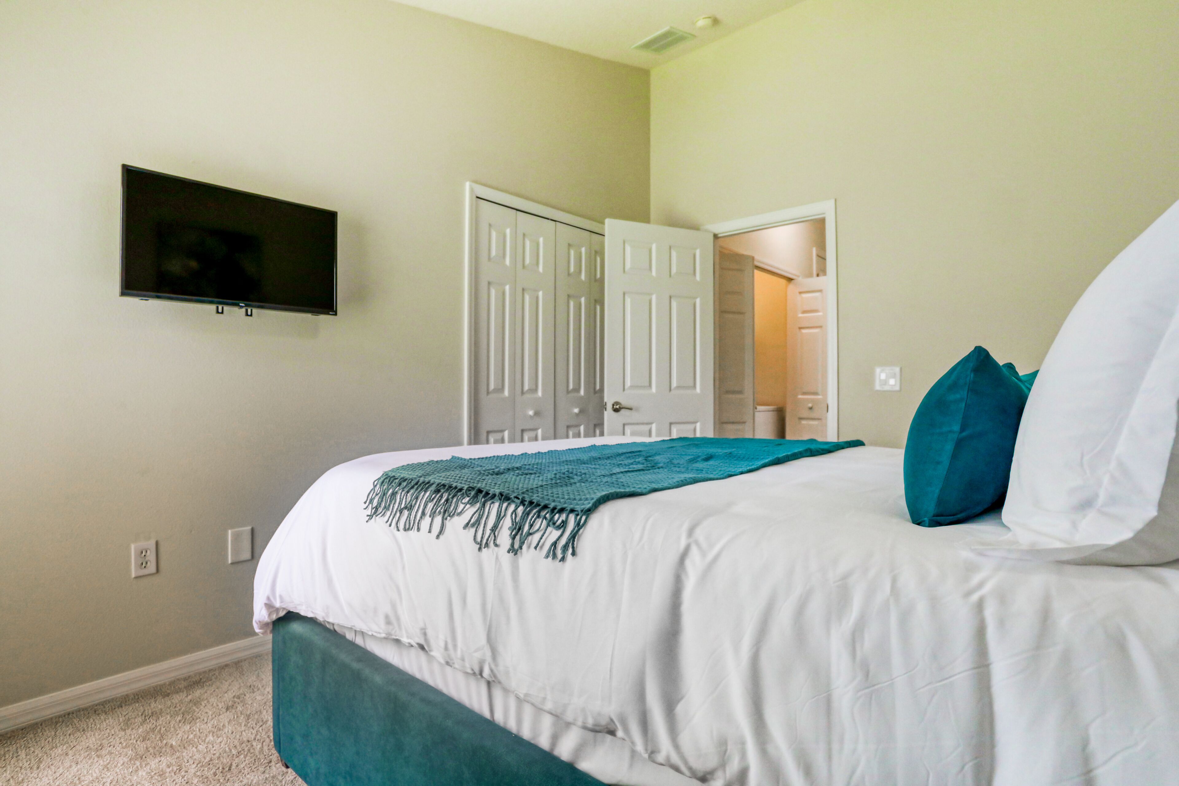 A bedroom with a bed, a television mounted on the wall, and a door leading to another room.