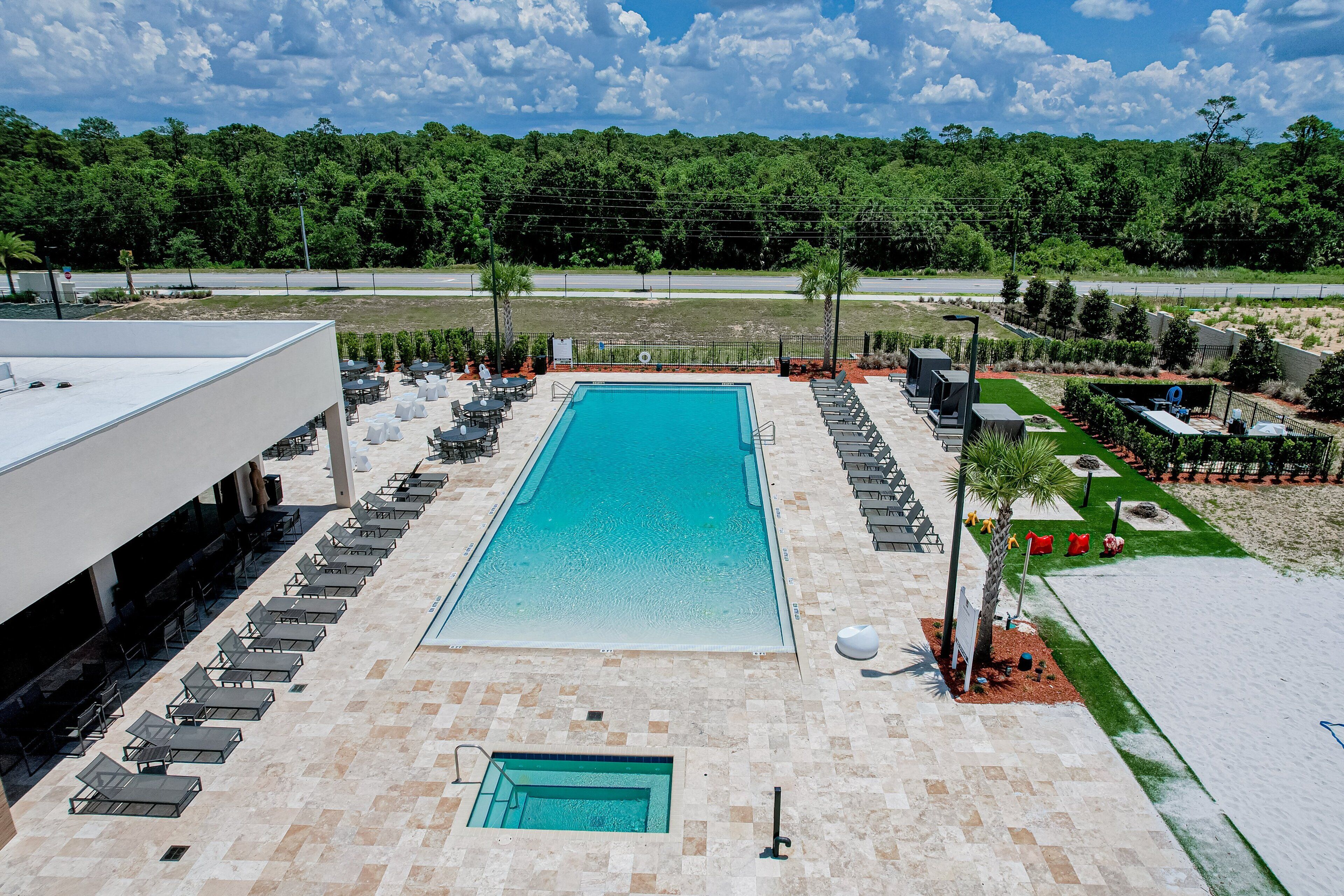A rectangular swimming pool with lounge chairs and a small pool area, surrounded by a landscaped garden and a road in the background.