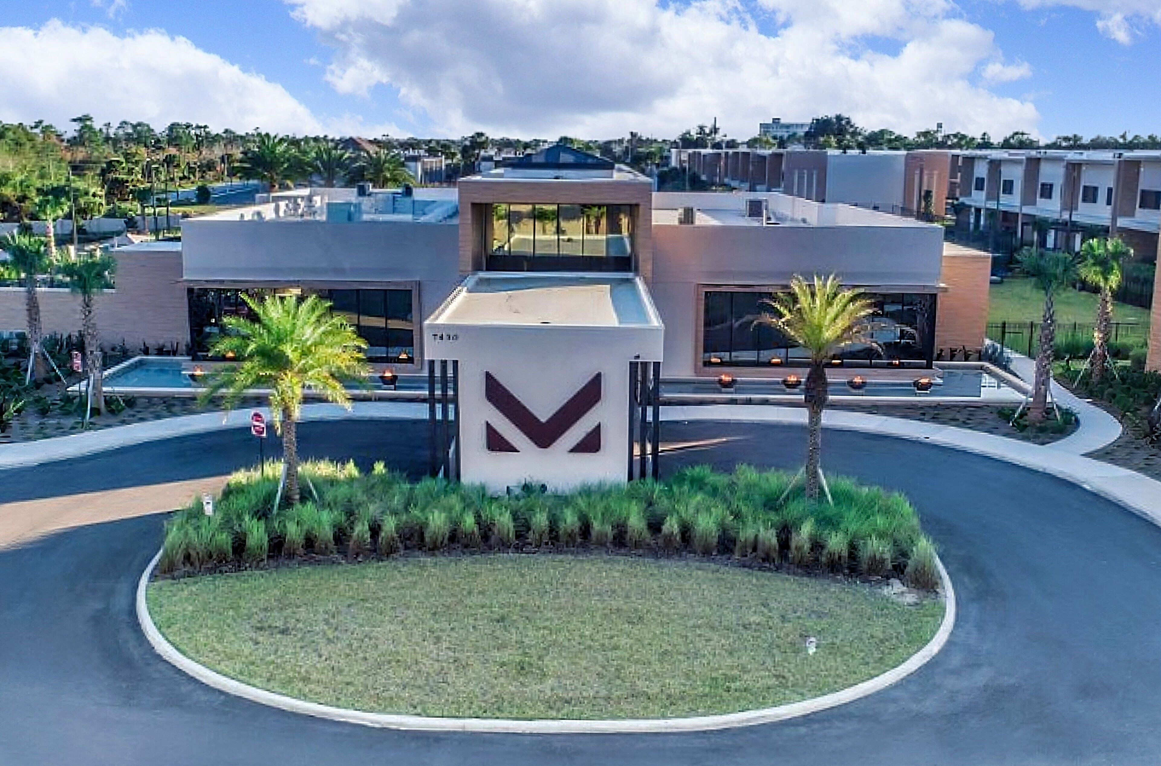 A modern hotel with a central courtyard, a large entrance with a distinctive logo, and a parking area.