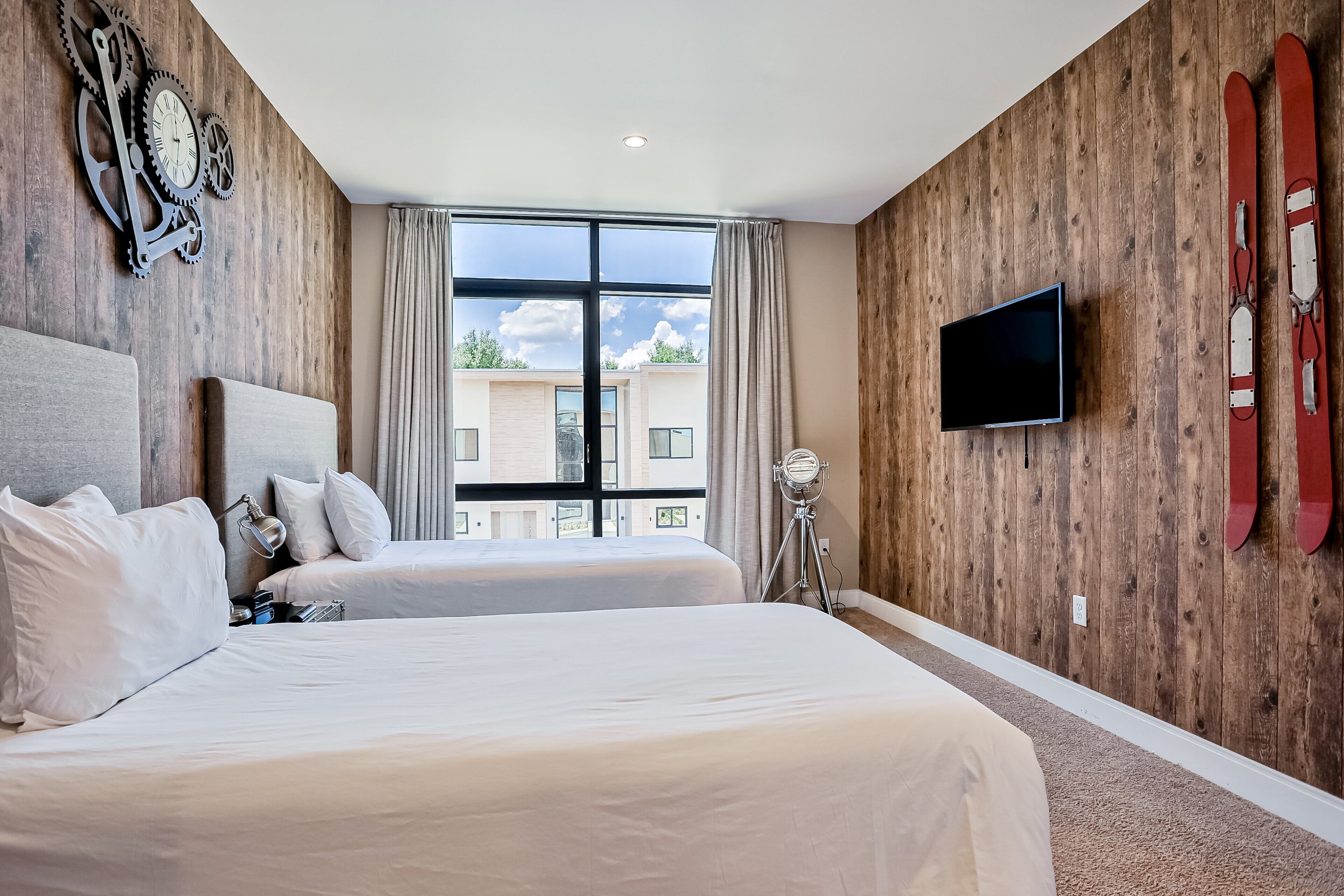 A hotel room with two beds, a TV, wooden walls, and a window with a view.
