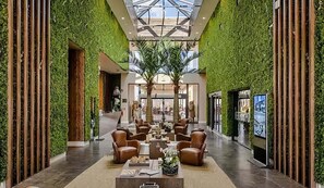 En hotellobby med et centralt siddeområde, grønne vægge og et højt til loftet.
