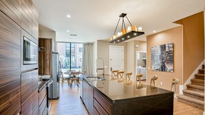 Een moderne keuken met houten kastjes, een centraal eiland en een eetgedeelte met stoelen.