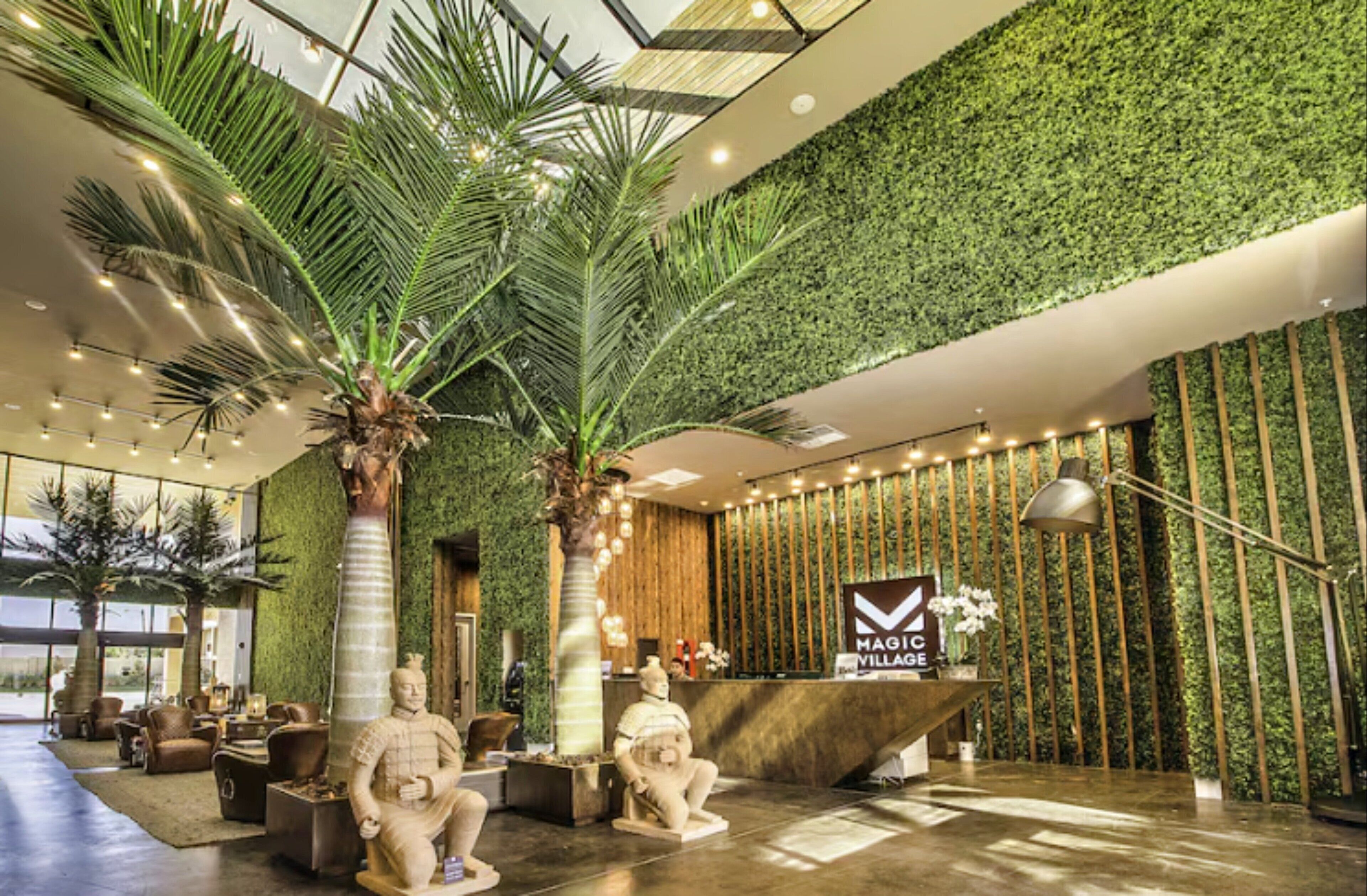 Eine moderne Lobby mit einer Rezeption, Palmen und einer grünen Wand.