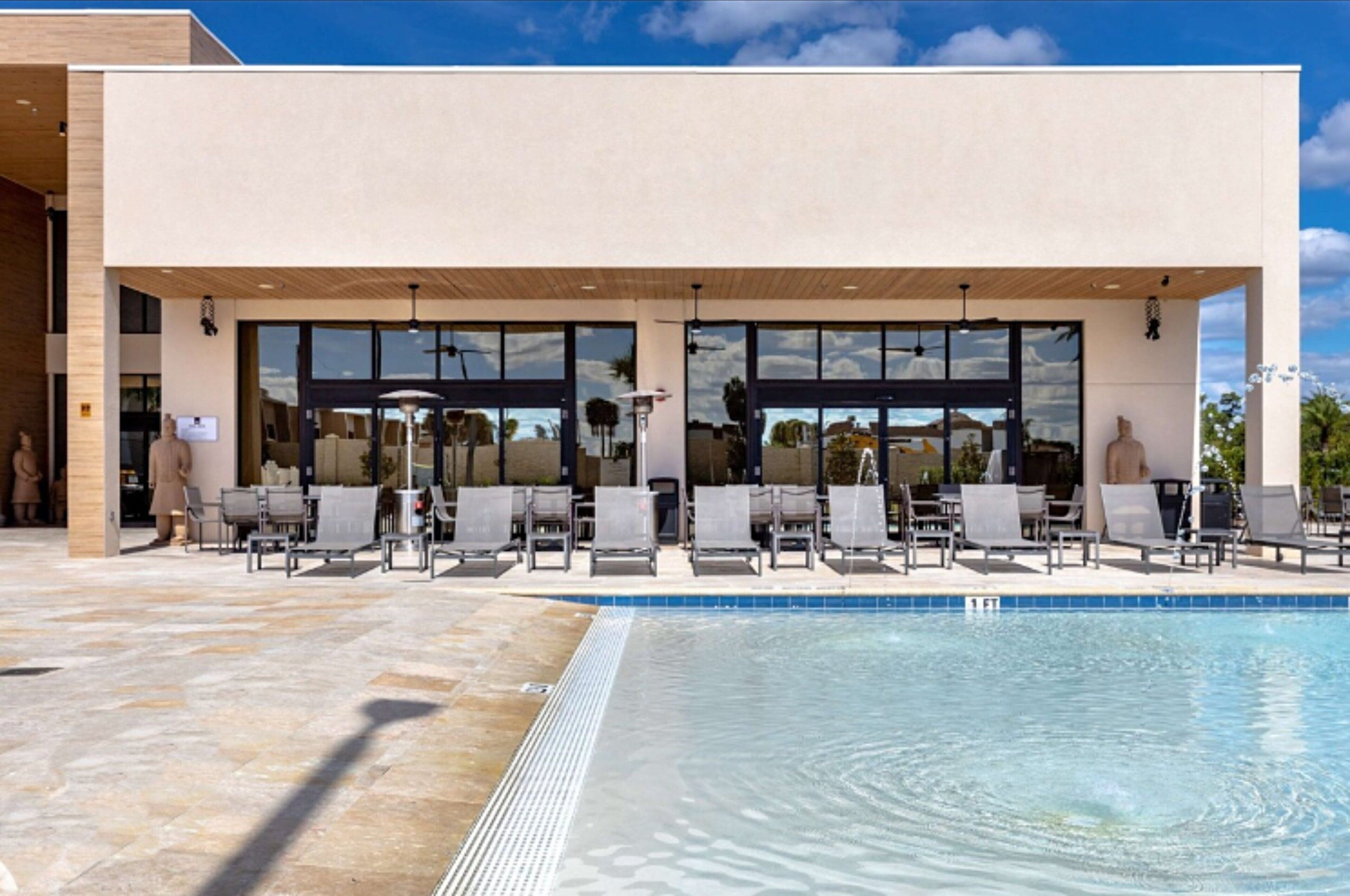 Un bâtiment moderne doté d’un espace piscine, comprenant des chaises longues et offrant une vue dégagée sur la piscine.