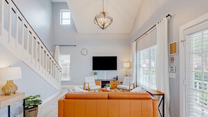 Een moderne woonkamer met een trap, een flatscreen televisie en een groot raam met zonwering.