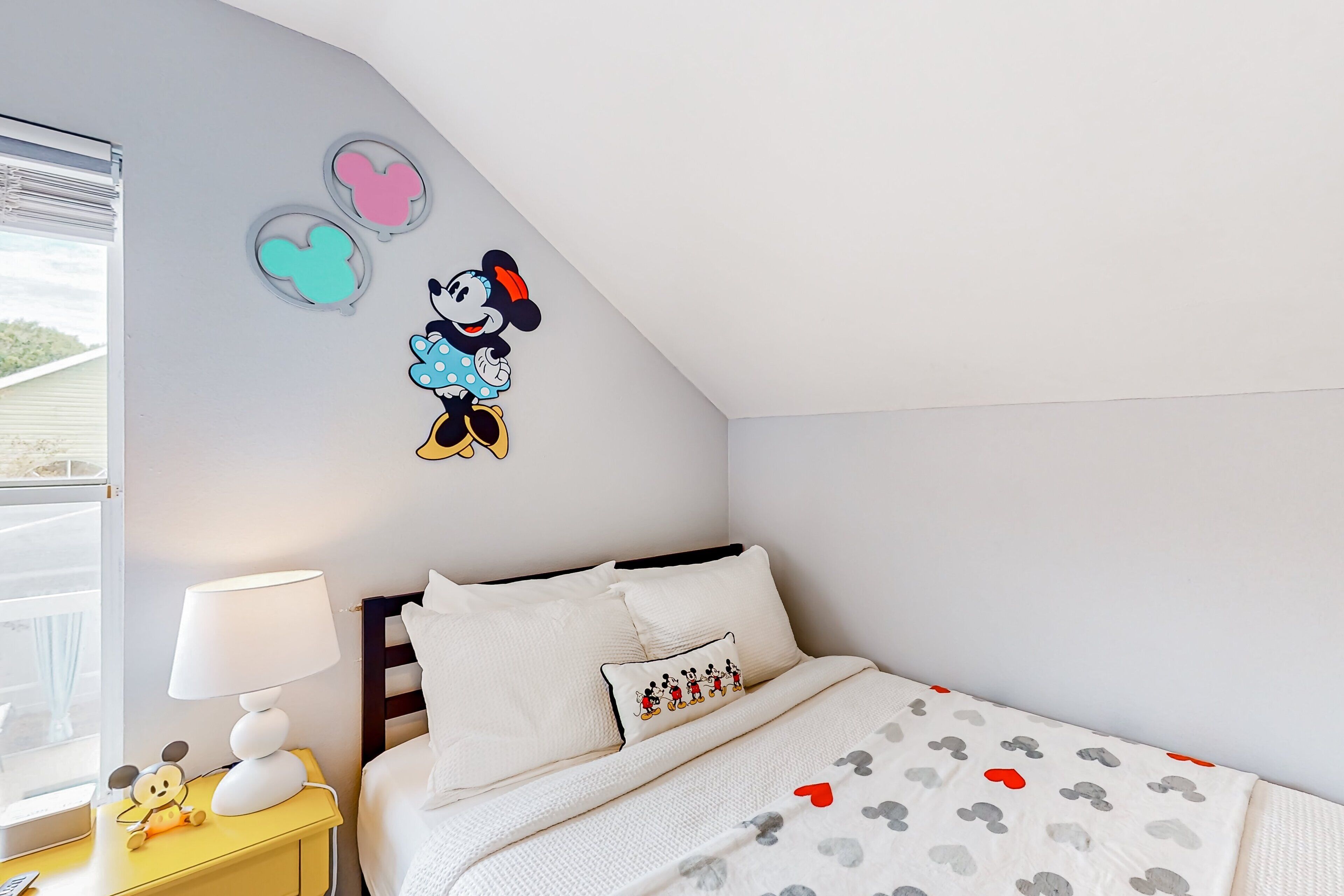 A bedroom with a bed, pillows, a nightstand, a lamp, and wall decorations.