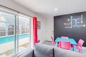 Ein Zimmer mit Pool, einer Glasschiebetür, einem blauen Tisch mit rosafarbenen Stühlen und einer Tafel mit Spielsteinen.