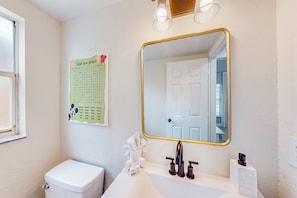 Ein Badezimmer mit Toilette, einem Waschbecken mit goldfarbenem Spiegelrahmen und einer an der Wand befestigten Liste.