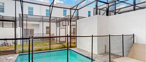 A modern outdoor pool area with a glass enclosure, a lounge chair, and a view of the surrounding buildings.